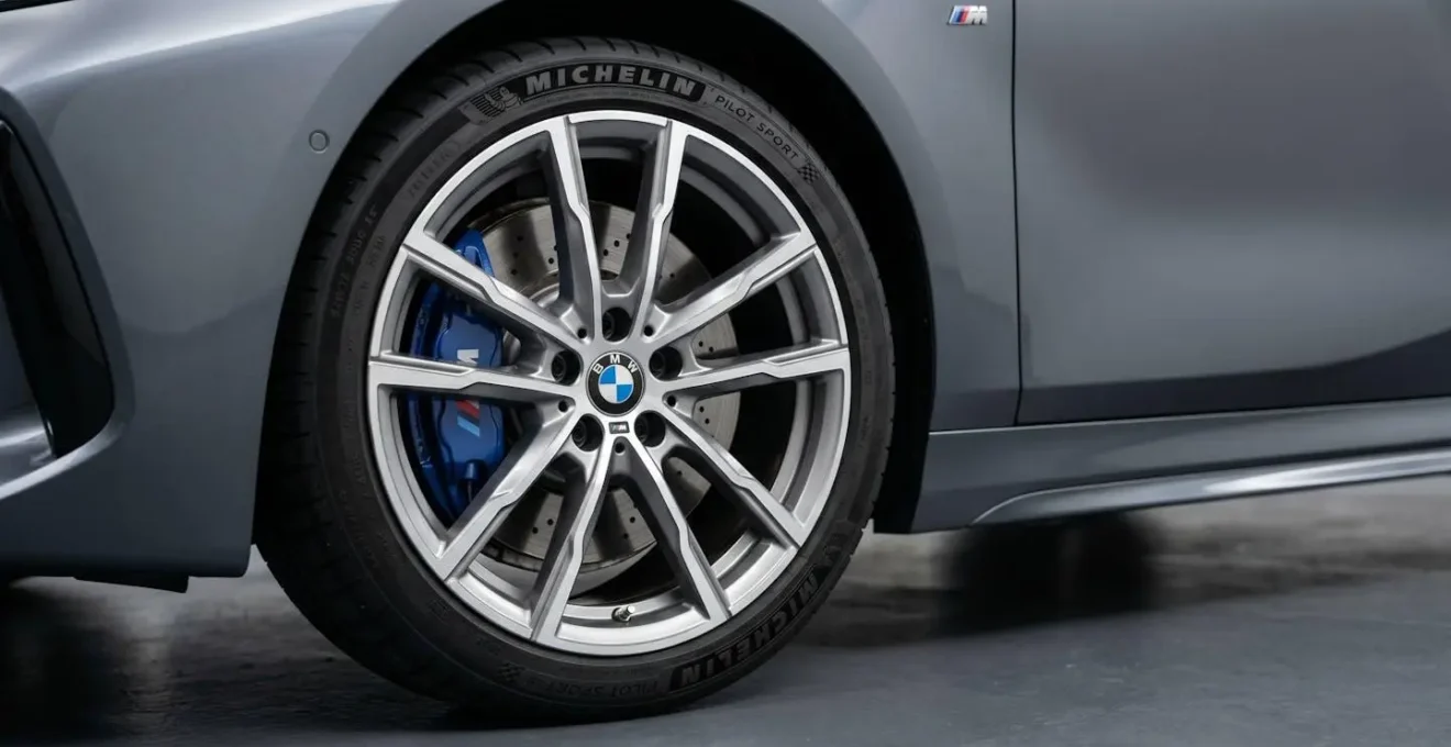 Gros plan sur jante alliage 18 pouces M Sport d'une BMW série 1 gris métallisé, étrier de frein bleu visible, badge M Sport sur bas de caisse en arrière-plan